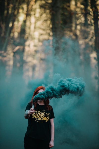 女人拿着汽化器释放蓝烟在森林附近
